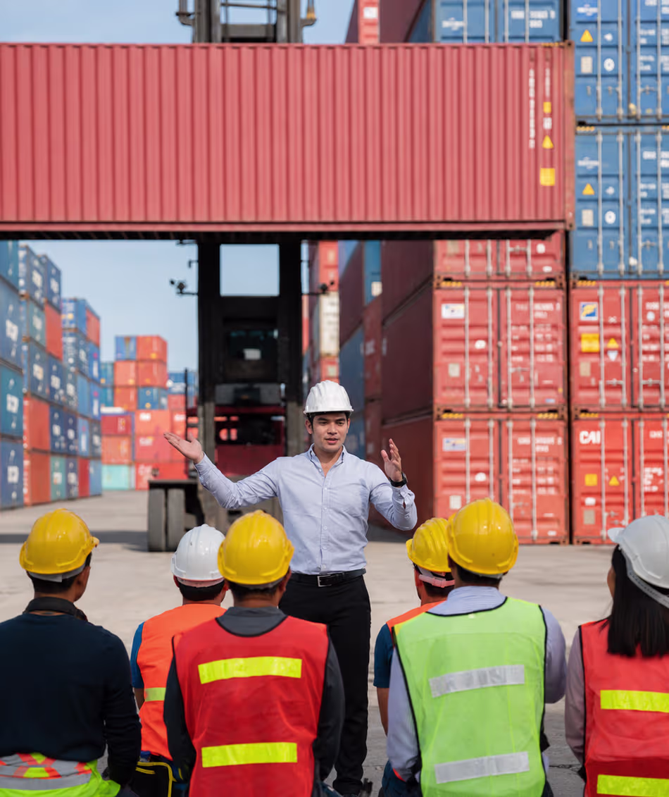 Logistics and container yard workers attending a workplace safety and operations briefing at an Australian freight and shipping terminal.